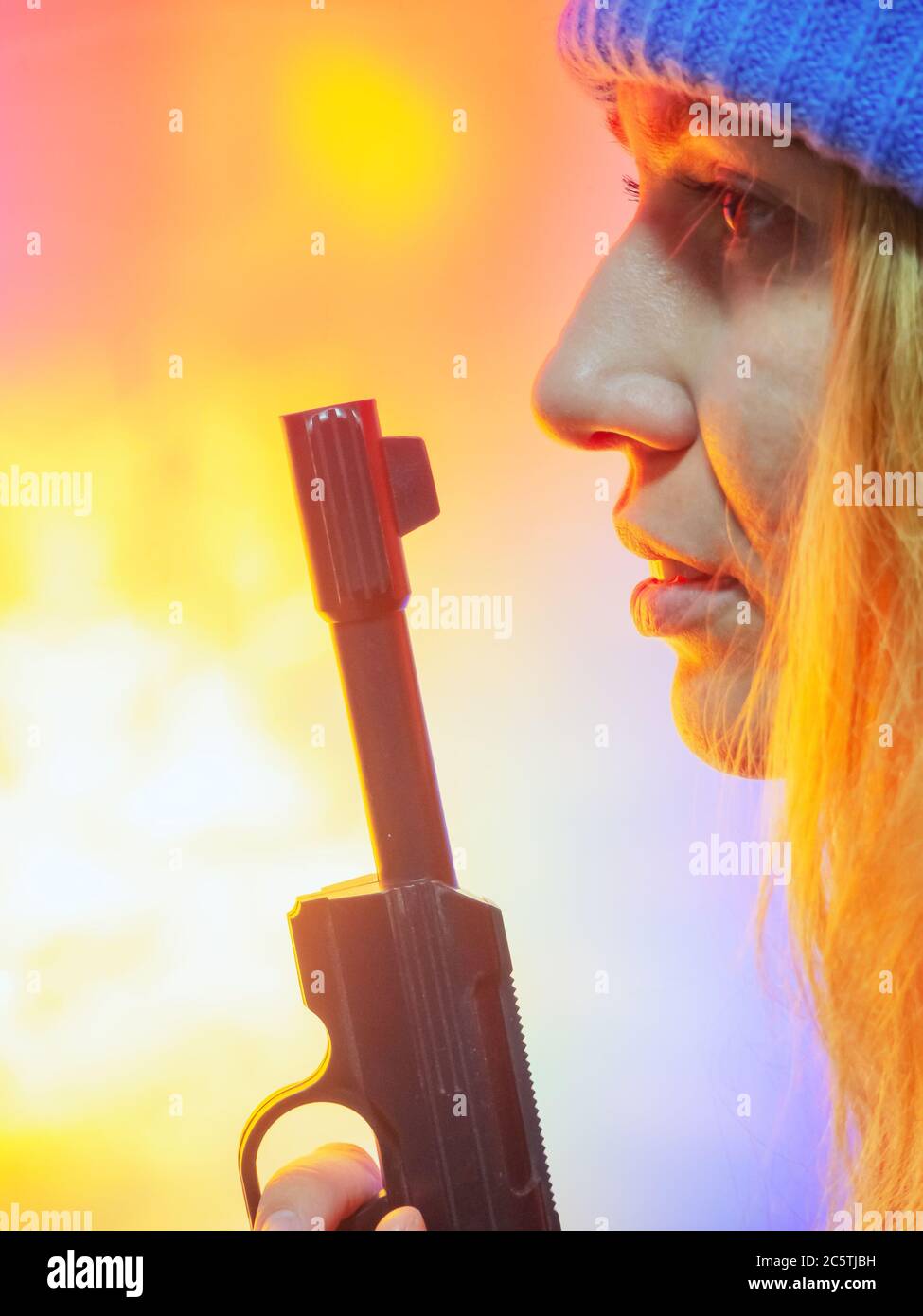 Ragazza di Provil in un cappello blu che tiene vicino alla faccia un barile lungo di un rivoltatore sovietico su uno sfondo colorato simile ad un'esplosione Foto Stock