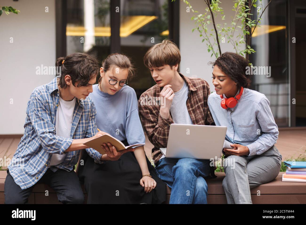 Foto degli studenti seduti su una panchina con un computer portatile e prenotati mentre si passa il tempo nel cortile dell'università Foto Stock