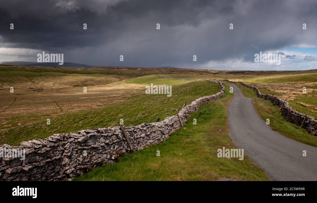 Una corsia di campagna si snoda tra pareti in pietra arenaria sulle colline brughiera di pecore a Cowgill Head sopra Garsdale e Dentdale nello Yorkshire D in Inghilterra Foto Stock