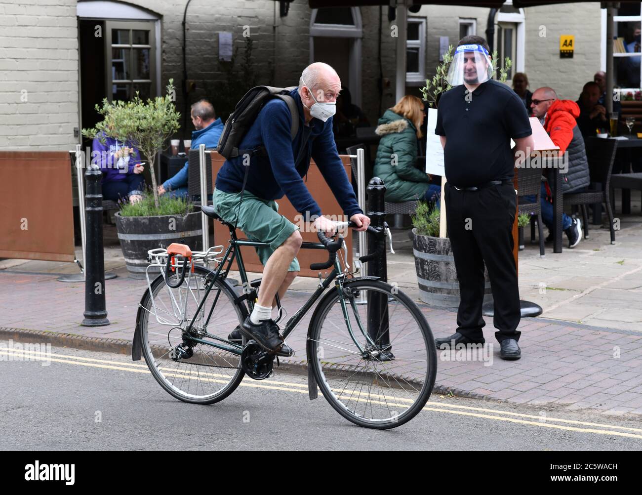 Ironbridge, Shropshire, Regno Unito 5 luglio 2020. Tempi strani come pub, ristoranti e negozi riaprono un membro del personale al pub White Hart indossa una visiera mentre attende di accogliere i clienti mentre passa un ciclista che indossa la maschera. Credit: David Bagnall/Alamy Live News Foto Stock