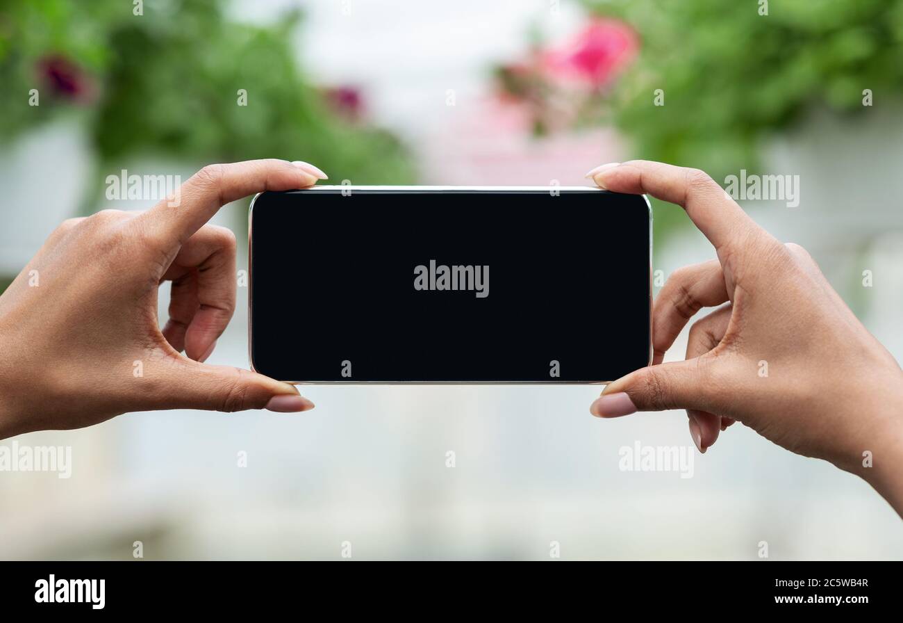 E-marketing e blog moderno sulle piante. African american girl fa fiori fotografici su pentole, all'interno di orangerie Foto Stock