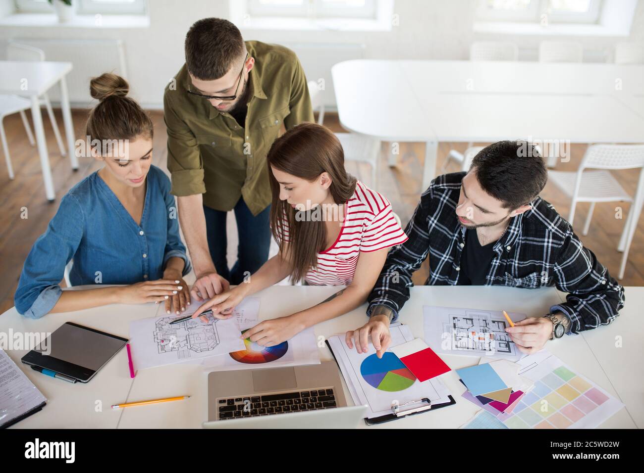 Gruppo di uomini e donne d'affari che lavorano con schizzi e computer portatile mentre si passa il tempo al lavoro. Giovani creativi discutono attentamente del lavoro Foto Stock