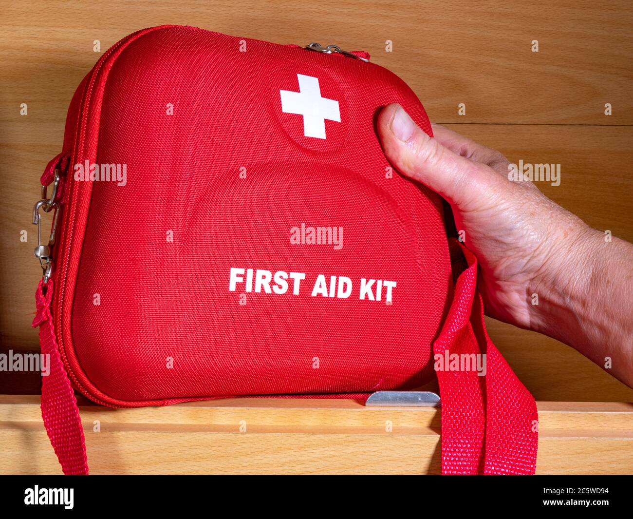 Primo piano di una mano di un uomo che raggiunge una scatola rossa di pronto soccorso in un armadio a muro camper / caravan, su un ripiano. Foto Stock