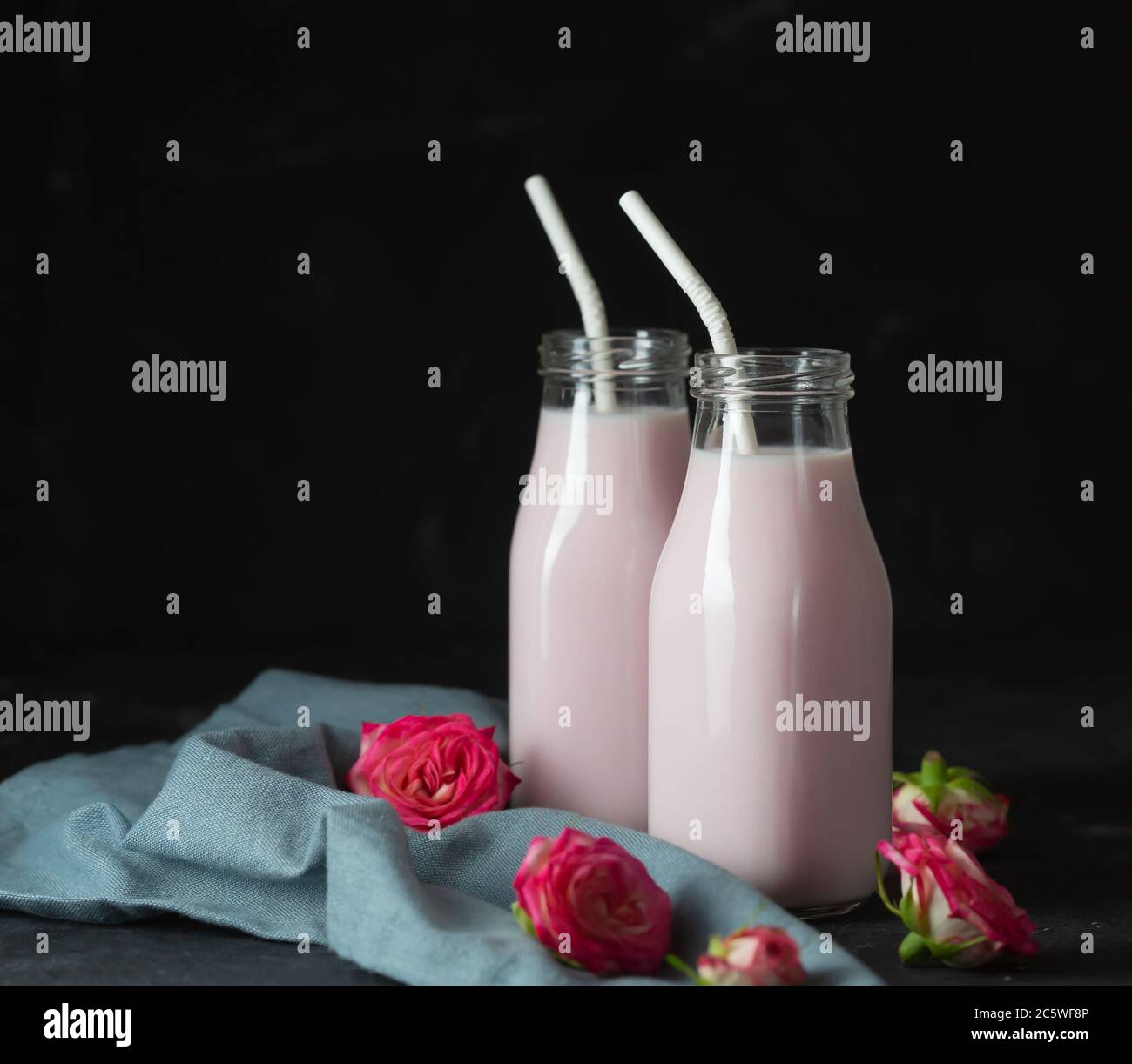 Il latte lunare si prepara con il fiore rosa in due bottiglie su sfondo nero. Drink rilassante alla moda a base di tradizioni ayurvediche Foto Stock