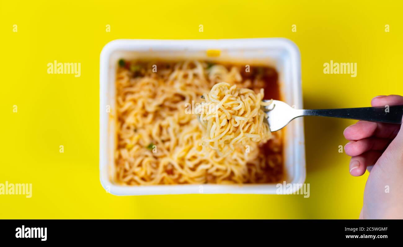 Primo piano di tagliatelle istantanee con spezie su sfondo giallo. Forchetta per agitare a mano da donna con maccheroni. Foto Stock