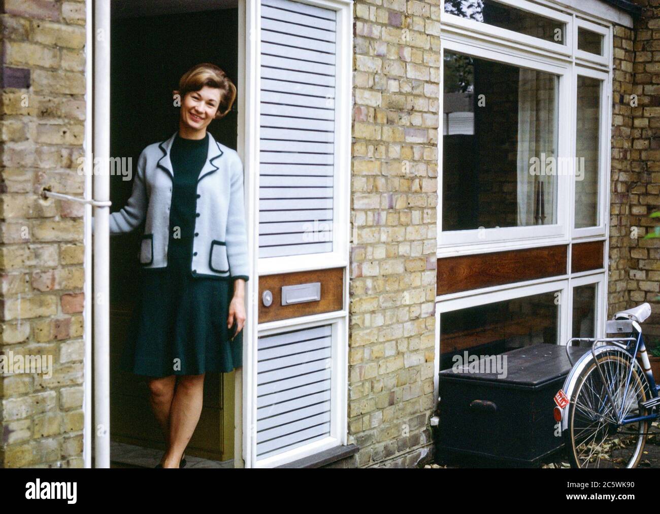 Bella donna che si trova nella porta d'ingresso di una casa di stile moderno a Hampstead, Londra, Inghilterra, Regno Unito negli anni '60 Foto Stock