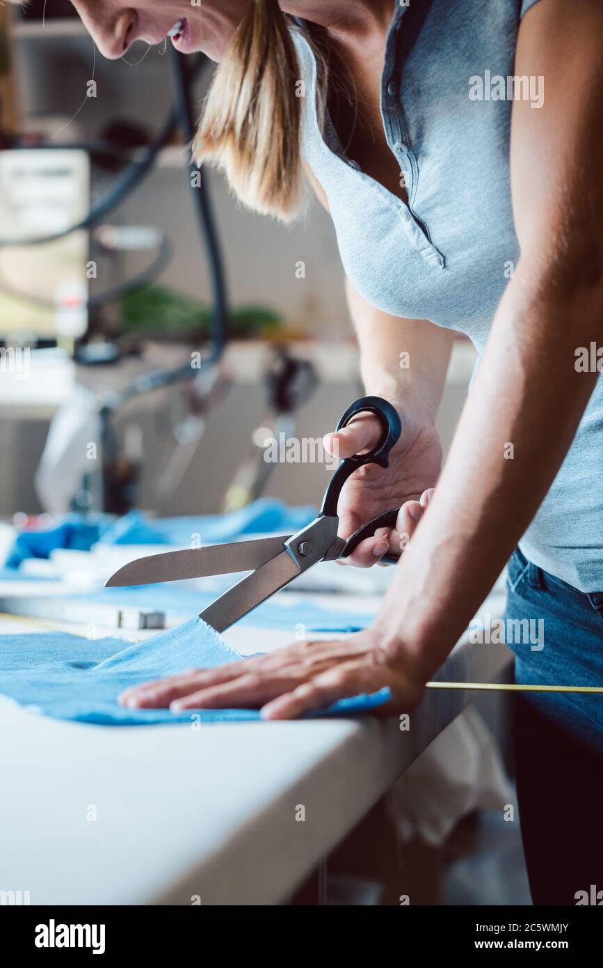 Donna che taglia il tessuto con forbici su misura sul tavolo di sarto Foto Stock