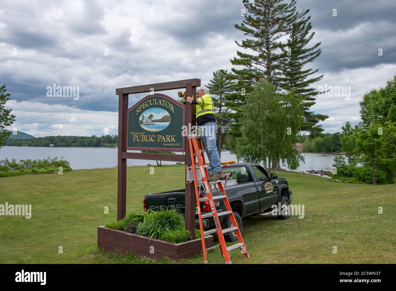 Un lavoratore in piedi su una scala che installa un cartello per lo Speculator Public Park sul lago Pleasant nelle Adirondack Mountains, NY USA Foto Stock