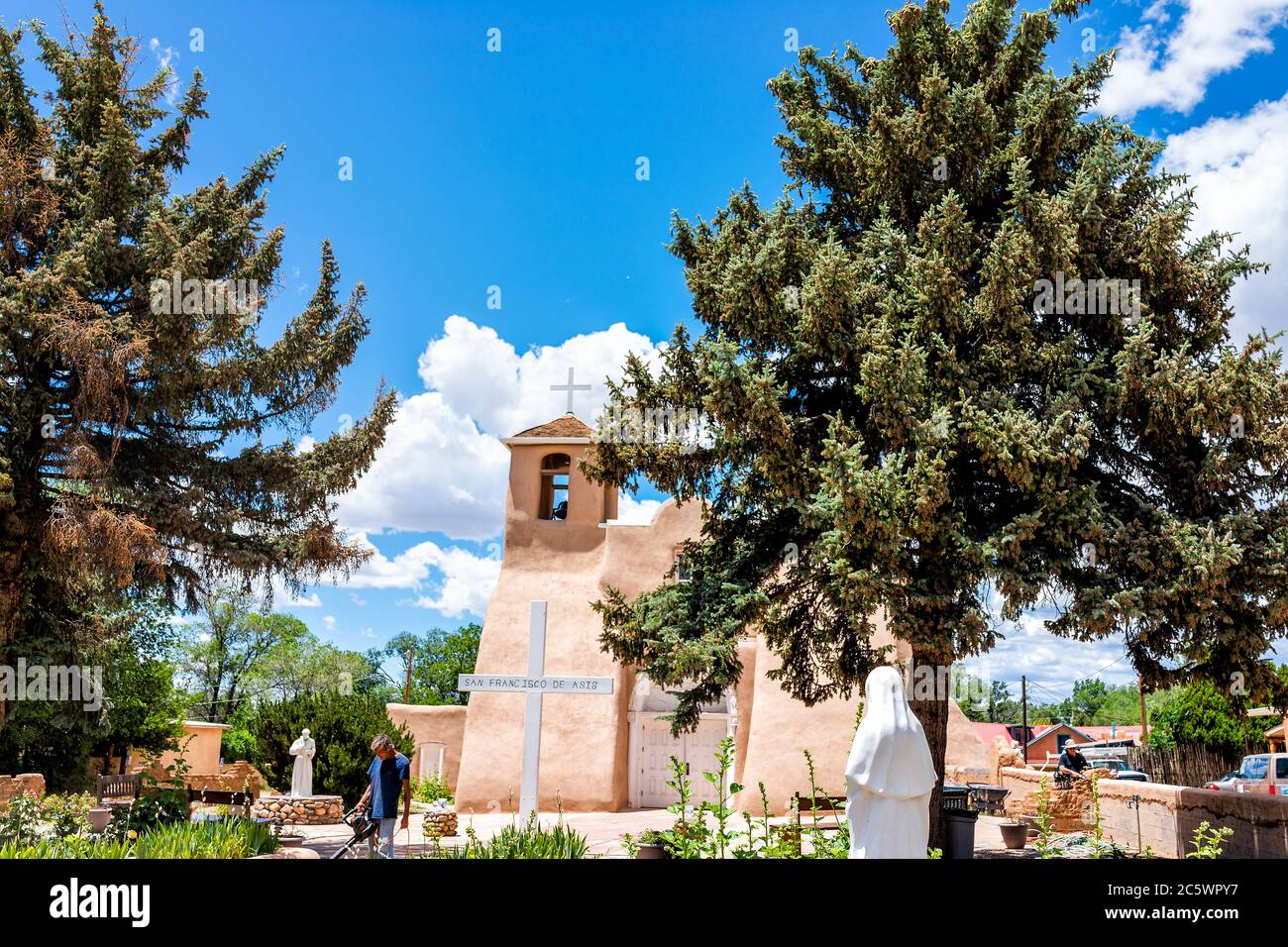 Ranchos de Taos, USA - 19 giugno 2019: St Francic Plaza e la chiesa di San Francisco de Aseis con la croce e l'uomo pulizia durante la ristrutturazione in corso Foto Stock