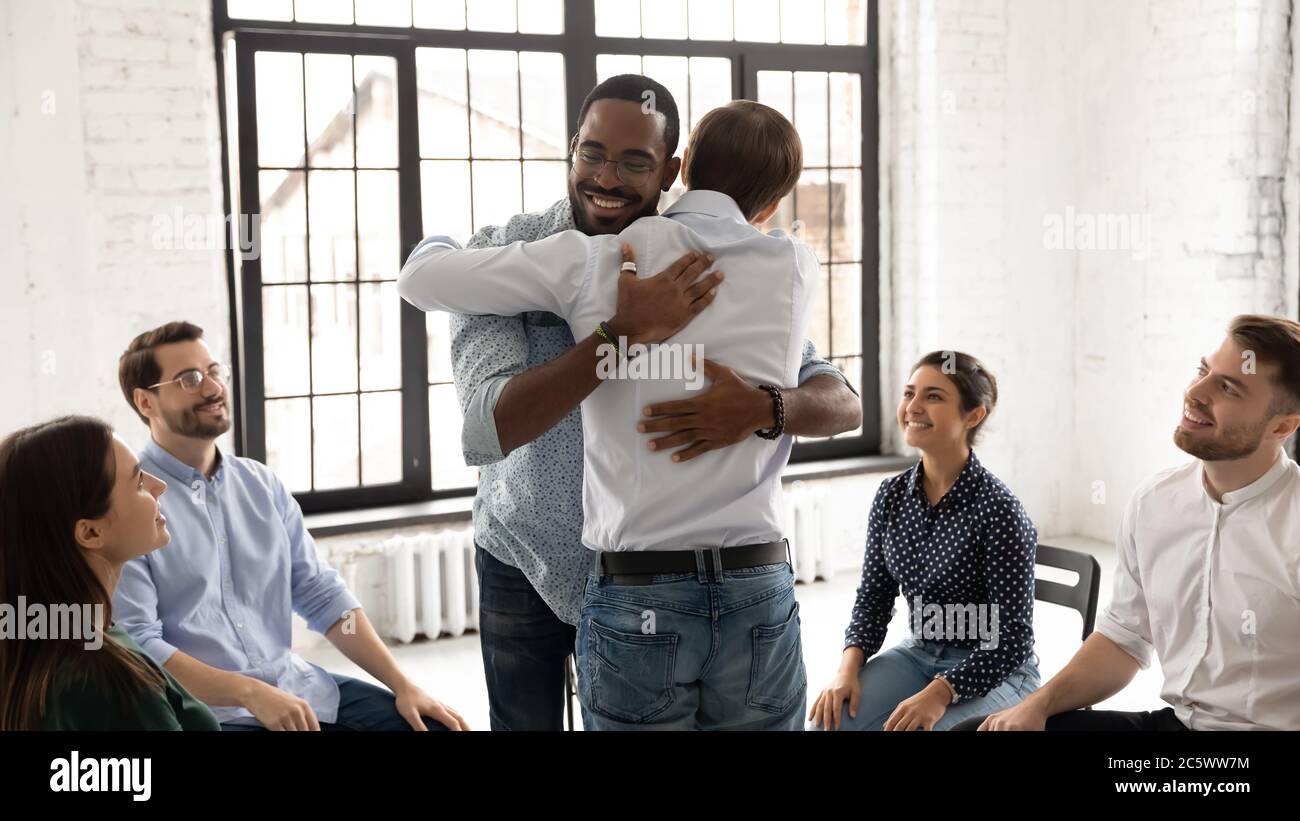 Uomini africani e caucasici che abbracciano durante la sessione di consulenza di terapia di gruppo Foto Stock