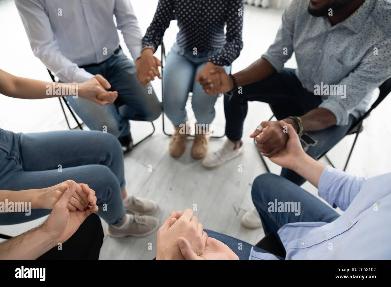 Persone che si siedono in cerchio tenendo le mani coinvolte nella terapia di gruppo Foto Stock