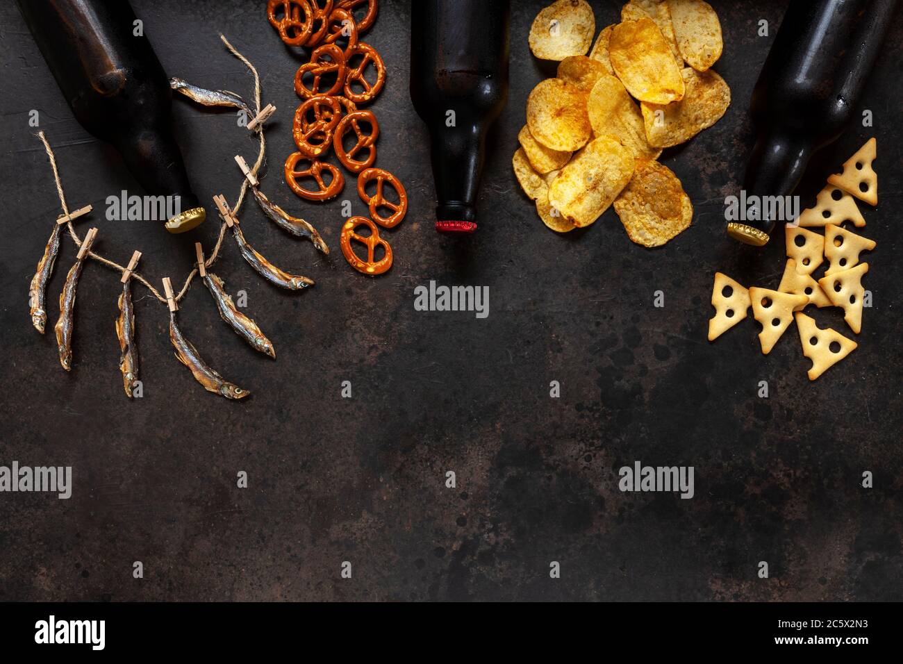 Tre bottiglie di birra con patatine, cracker salati, bretzel e pesce secco profumato Foto Stock