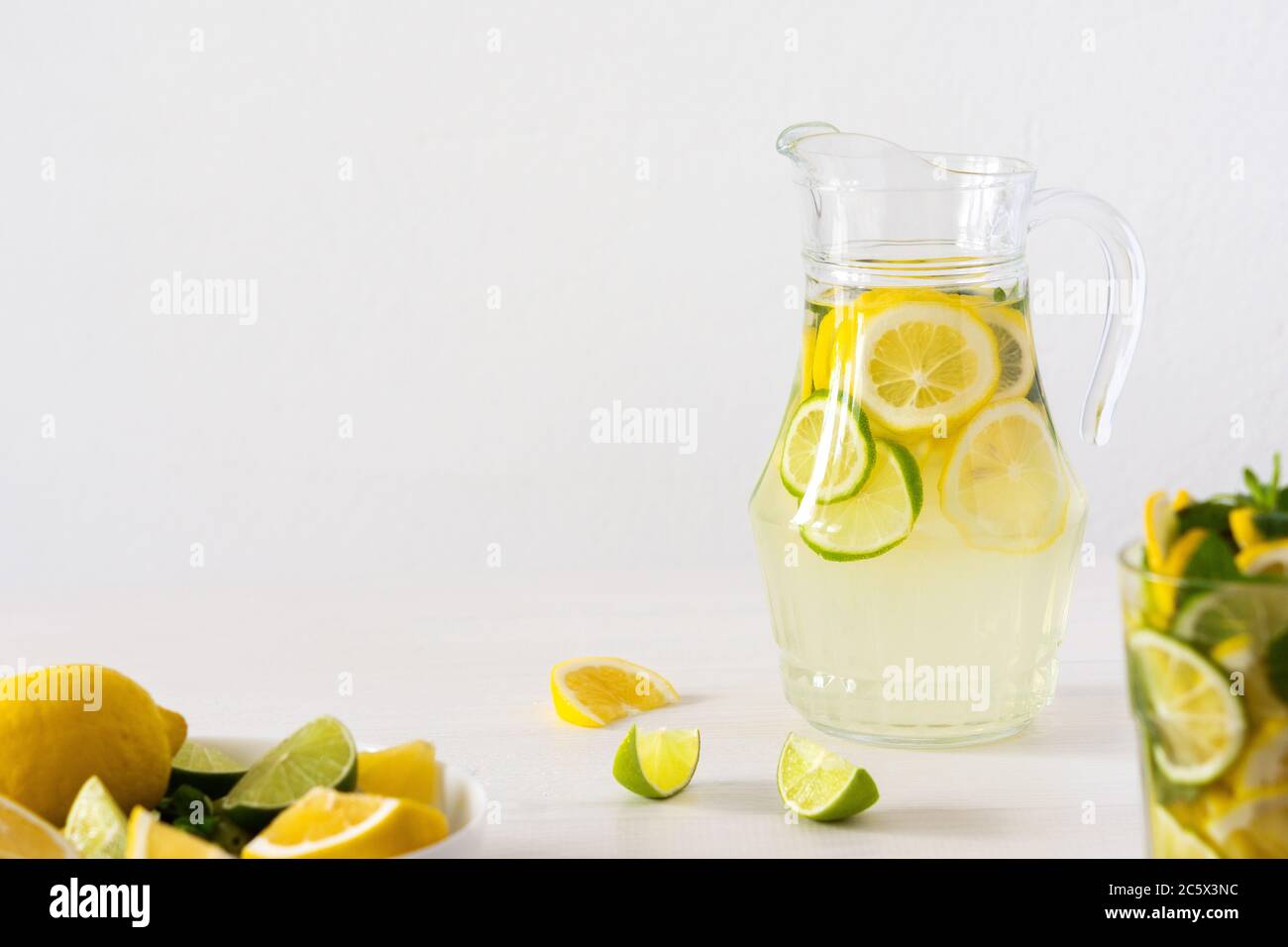 Bevanda estiva rinfrescante di limone, lime e menta, caraffa con limonata e bicchieri e fette di agrumi Foto Stock