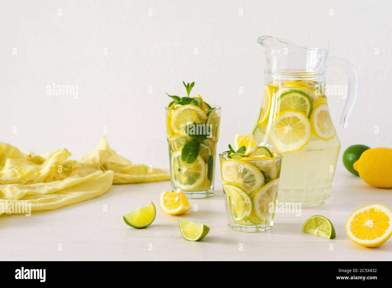 Bevanda estiva rinfrescante di limone, lime e menta, caraffa con limonata e bicchieri e fette di agrumi Foto Stock