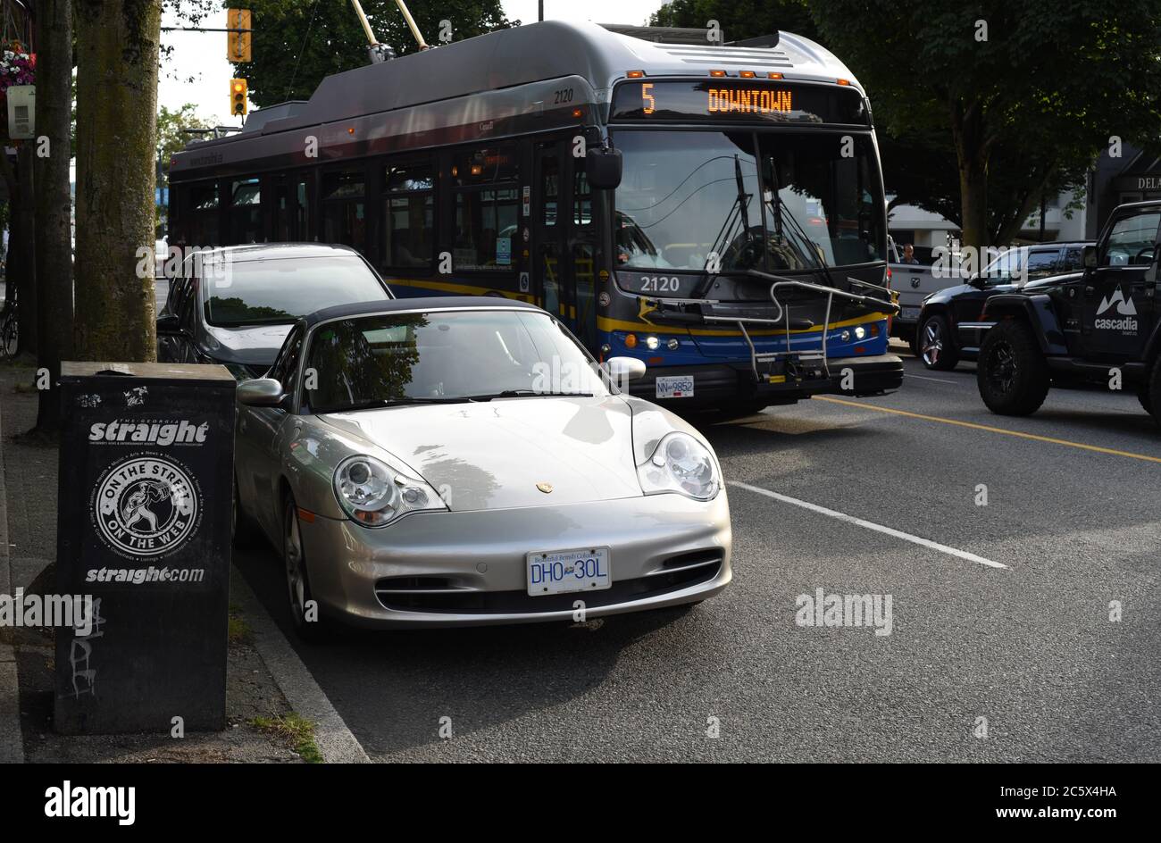 Un autobus Translink numero 5 passa tra il traffico e una Porsche parcheggiata e una cassetta di giornale per il giornale alternativo The Georgia Straight al Foto Stock