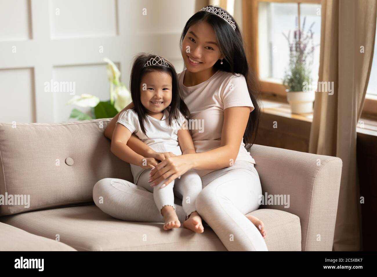 Sorridente giovane donna vietnamita coccolando piccola figlia carina bambino prescolare. Foto Stock