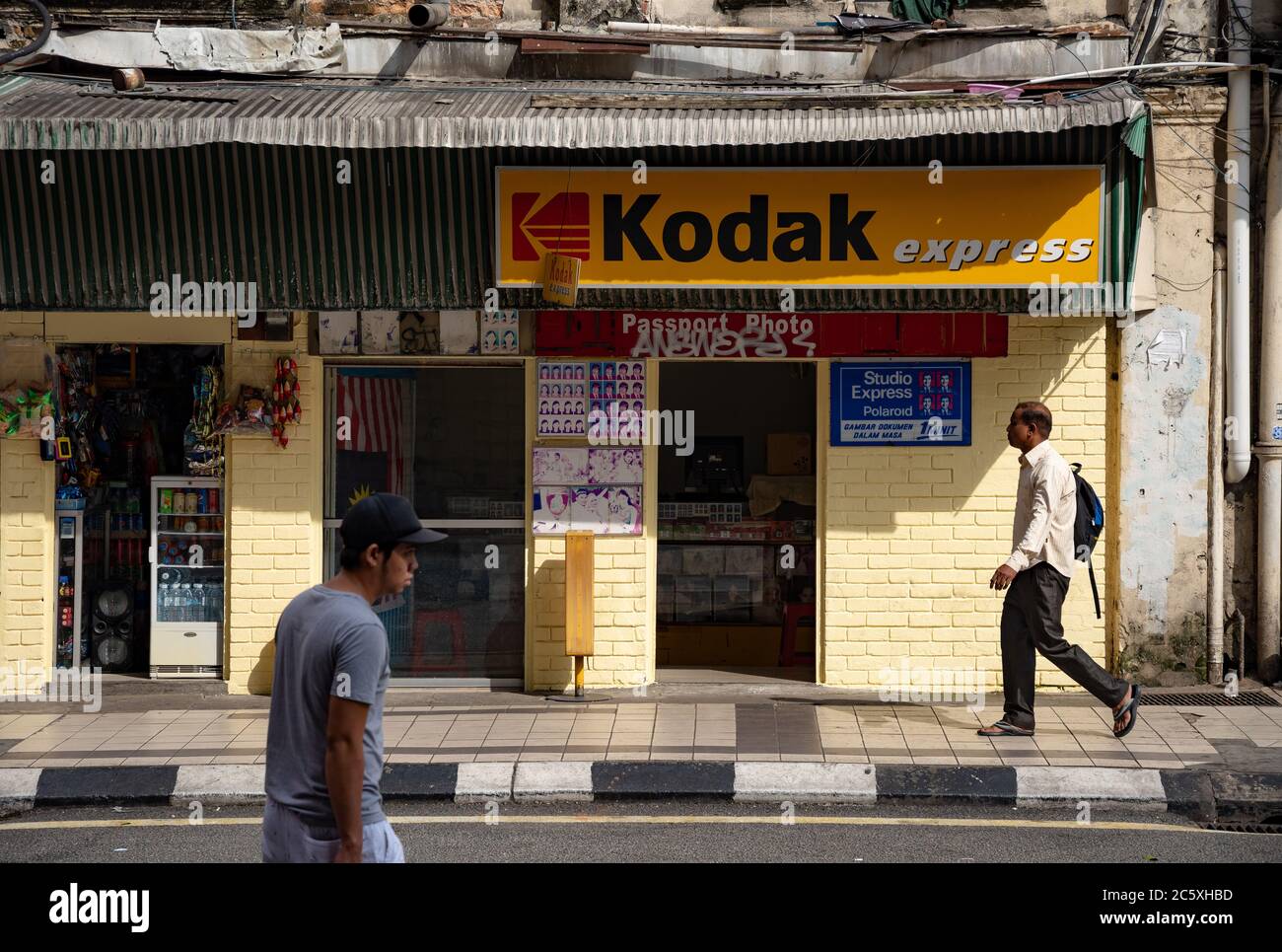 Street scene: vintage Kodak express store con una parete di mattoni gialli e uomini asiatici che passano a Kuala Lumpur. Foto Stock