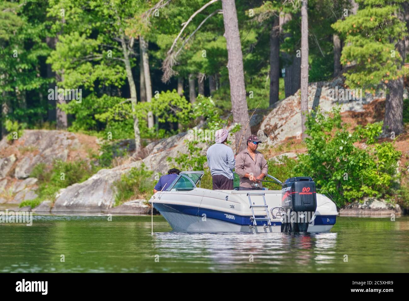 Tre uomini in una piccola barca di pesca sportiva in una giornata di sole a Stony Lake nella contea di Peterborough, Ontario, Canada. Foto Stock