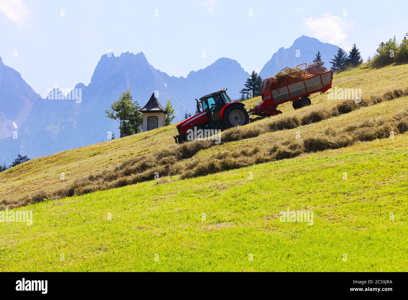 Romantico paesaggio rurale alpino con trattore che raccoglie fieno e nebbia montagne sullo sfondo con spazio per il tuo testo Foto Stock