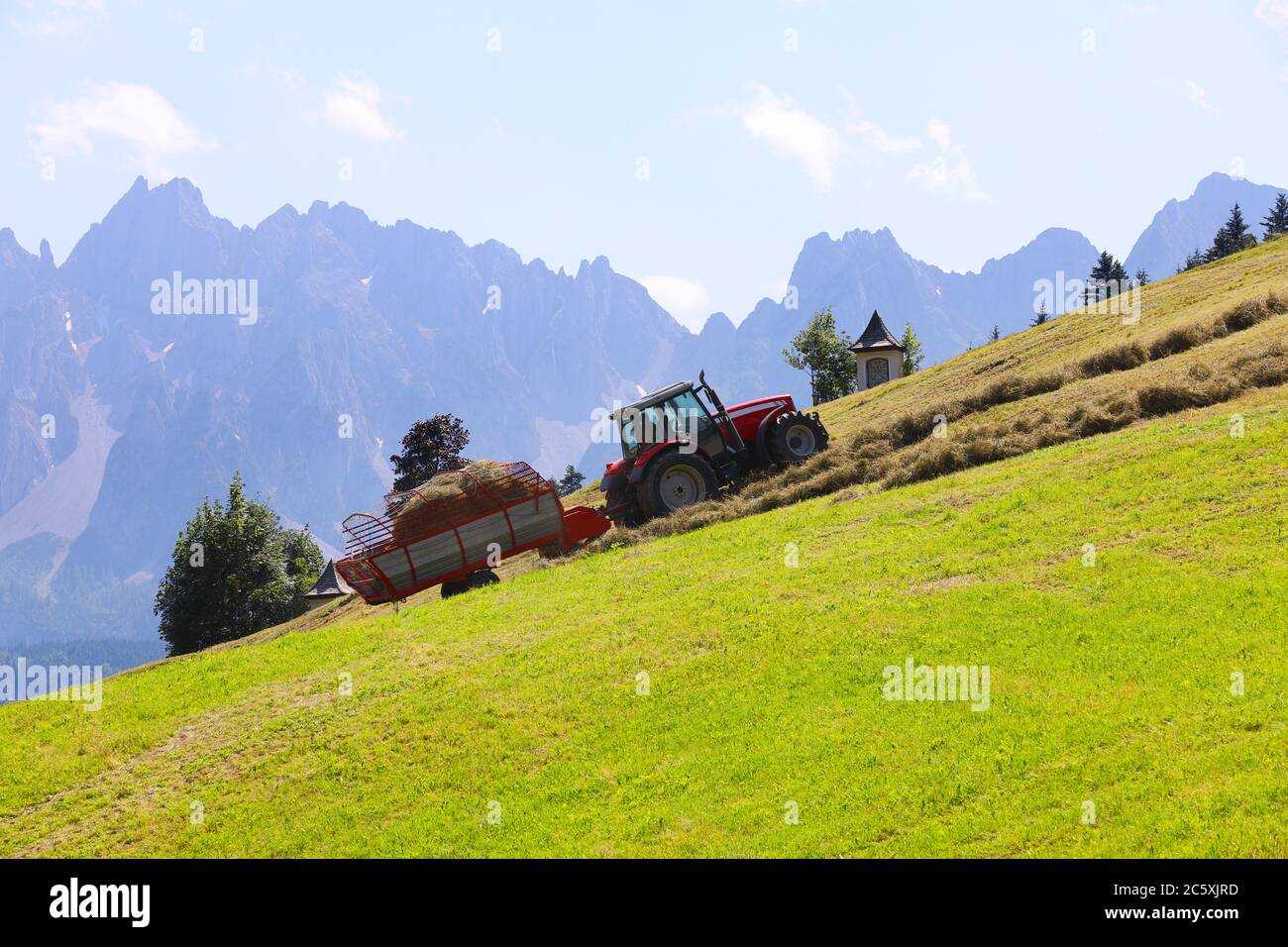 Romantico paesaggio rurale alpino con trattore che raccoglie fieno e nebbia montagne sullo sfondo con spazio per il tuo testo Foto Stock