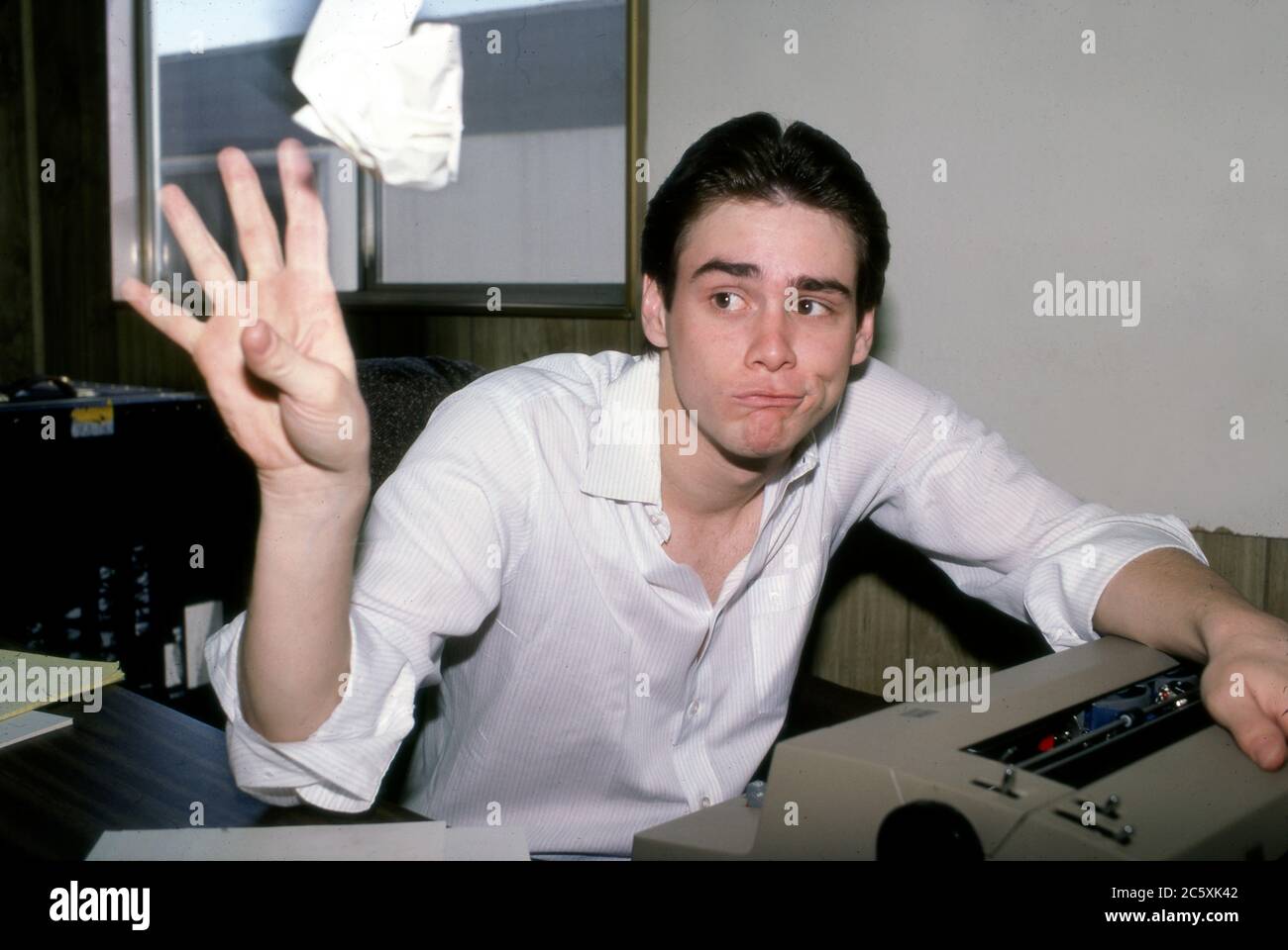 Un giovane Jim Carrey che lancia una bozza rifiutata dalla sua macchina da scrivere alla scrivania dell'ufficio mentre finge di essere uno scrittore al lavoro. Foto Stock