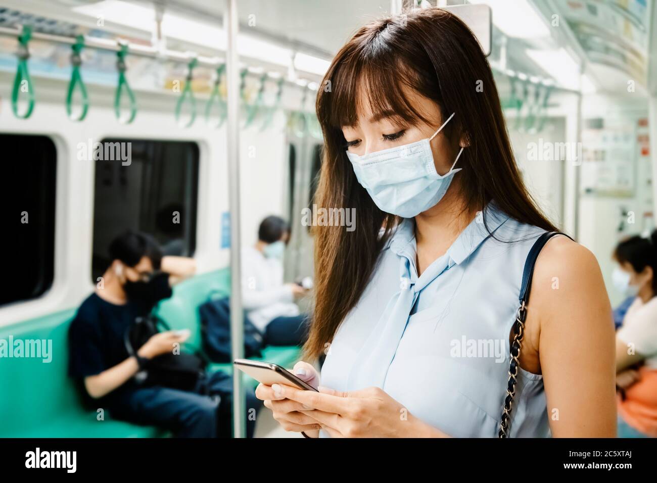 Giovane donna asiatica passeggero con maschera chirurgica e telefono cellulare in treno della metropolitana Foto Stock