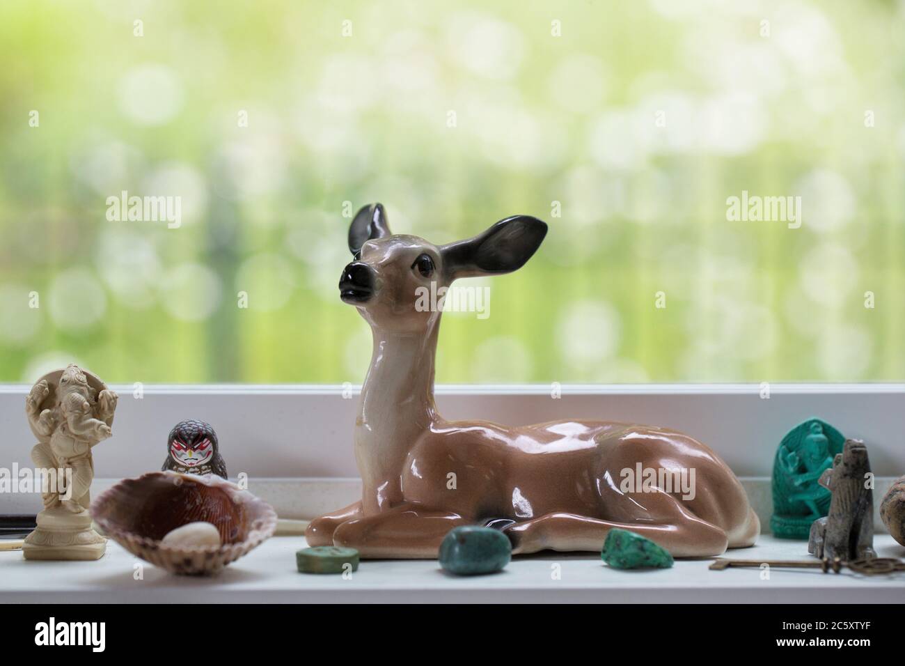 Una statuina vintage di cervo e altre rocce e talismani assortite, su un davanzale. Foto Stock