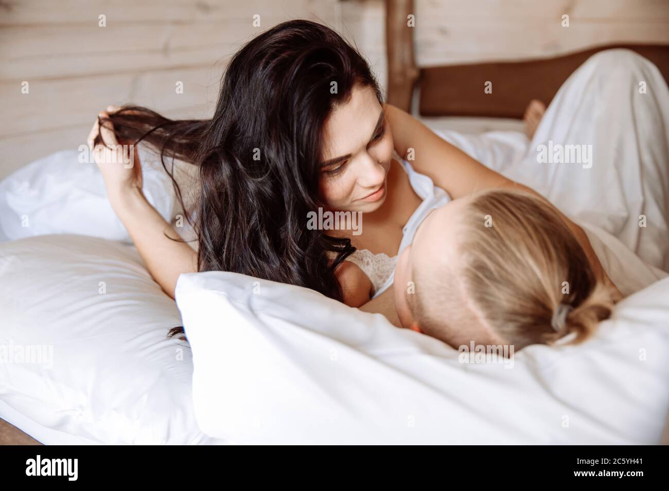 Un giovane uomo e una donna si stanno crogiolando a letto insieme. Sono stesi sotto un foglio bianco. Una coppia amorevole si è appena svegliata. Foto Stock