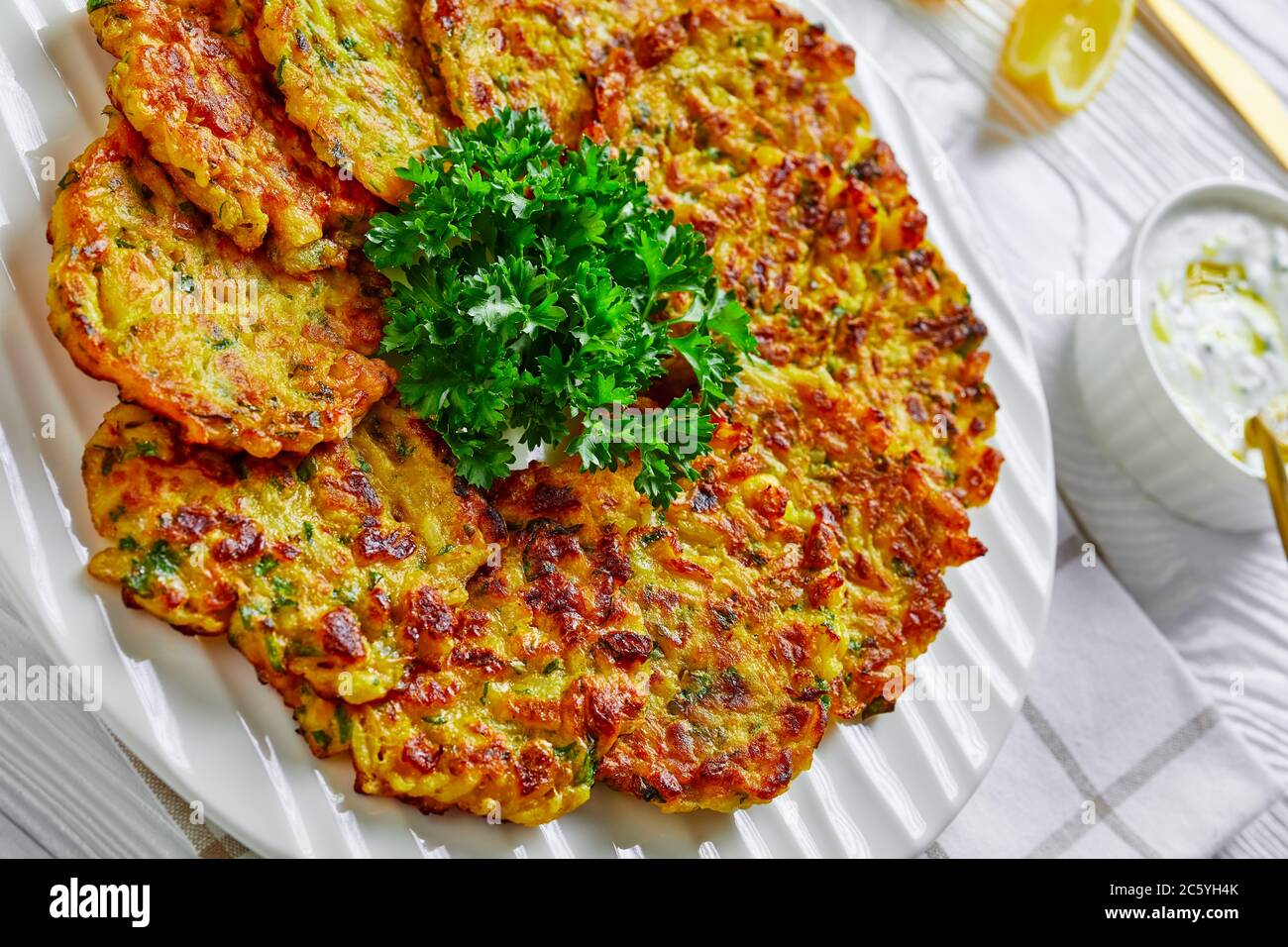 Cibo ebraico: Fiocchi di cipolla dolci o frittelle con verdure e riso, serviti su un piatto bianco con prezzemolo e salsa allo yogurt su fondo bianco di legno, Foto Stock