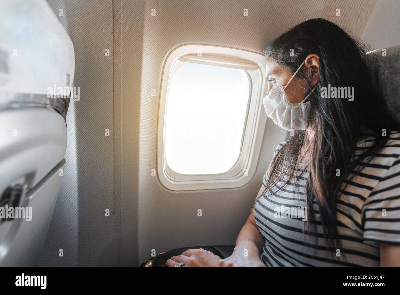 Giovane donna con maschera di protezione è seduta in aereo e guardando la vista dalla finestra. Interruzione del virus corona. Foto di alta qualità Foto Stock