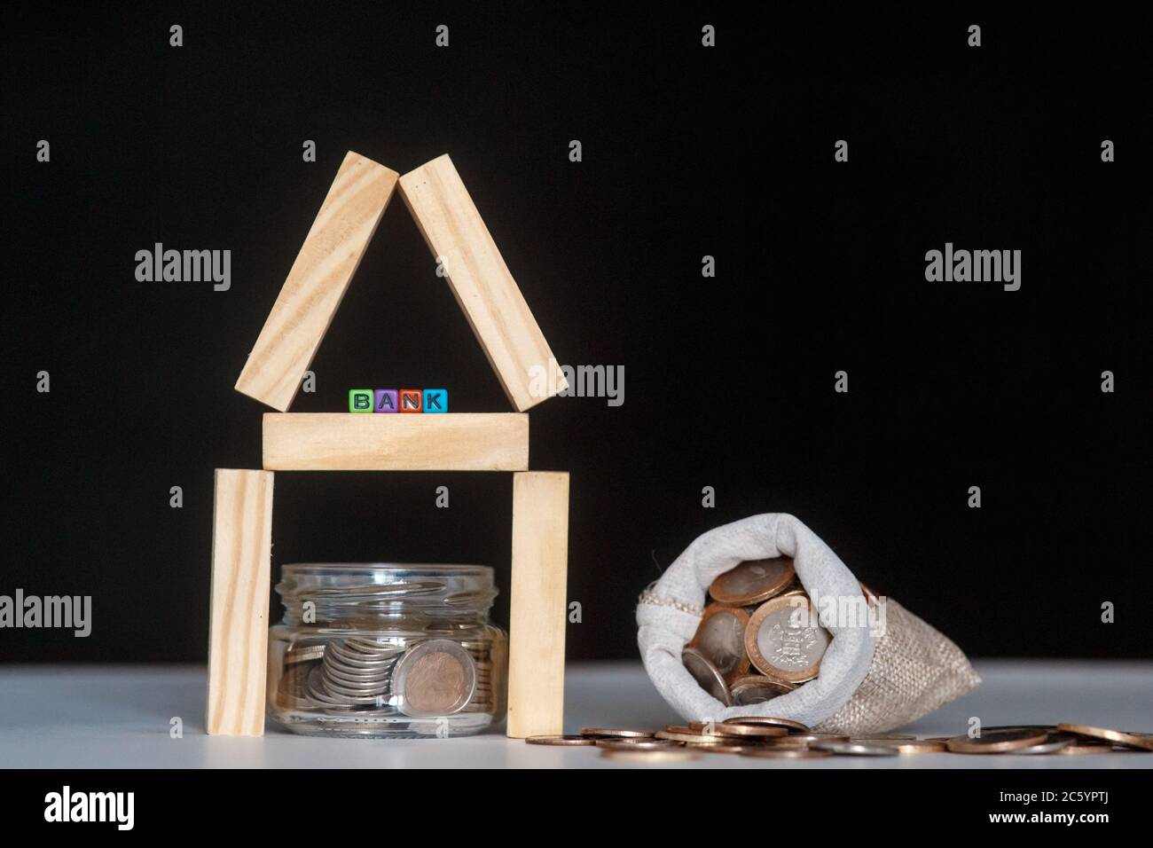 Banca di vetro con molte monete del mondo, parola o etichetta della casa su vaso di denaro e blocchi geometrici della casa di legno sopra la tabella Foto Stock