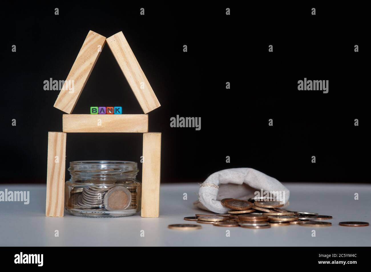 Banca di vetro con molte monete del mondo, parola o etichetta della casa su vaso di denaro e blocchi geometrici della casa di legno sopra la tabella Foto Stock