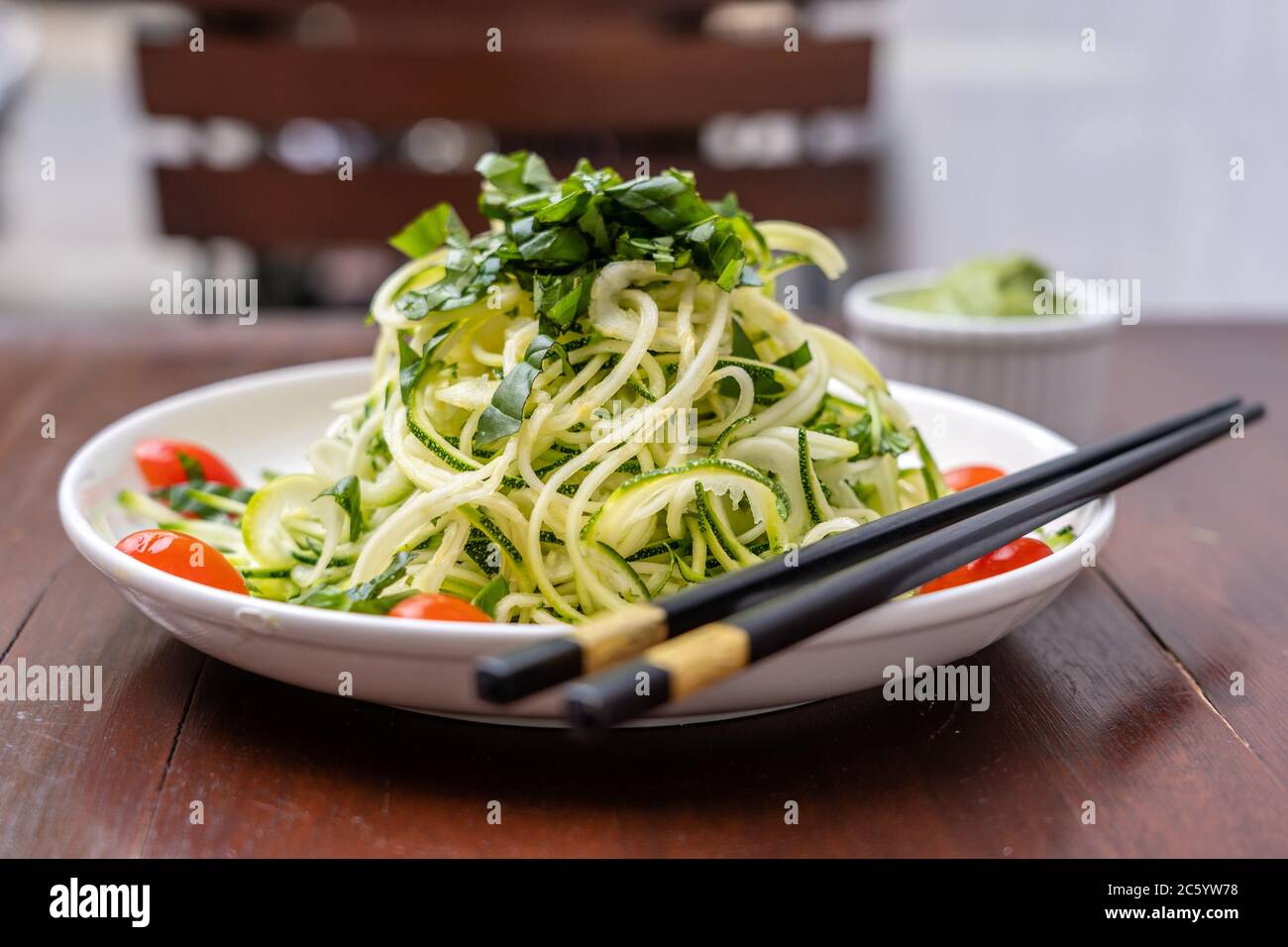 Tagliatelle di zucchine spiralizzate, cetrioli, pomodori ciliegini, aglio in un pesto cremoso di avocado. Cibo crudo per vegetariani. Primo piano Foto Stock