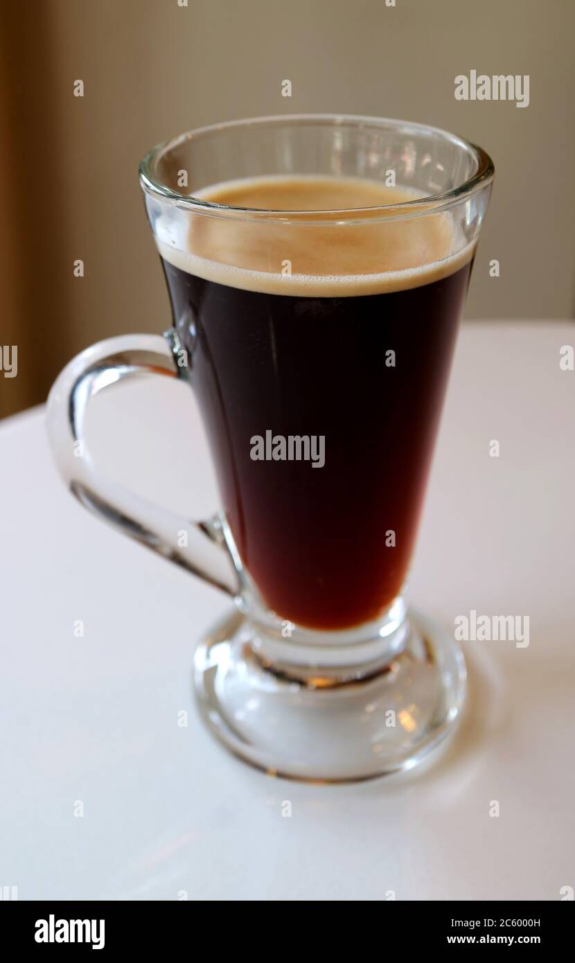 Immagine verticale di caffè nero caldo in un vetro trasparente isolato su un tavolo bianco Foto Stock