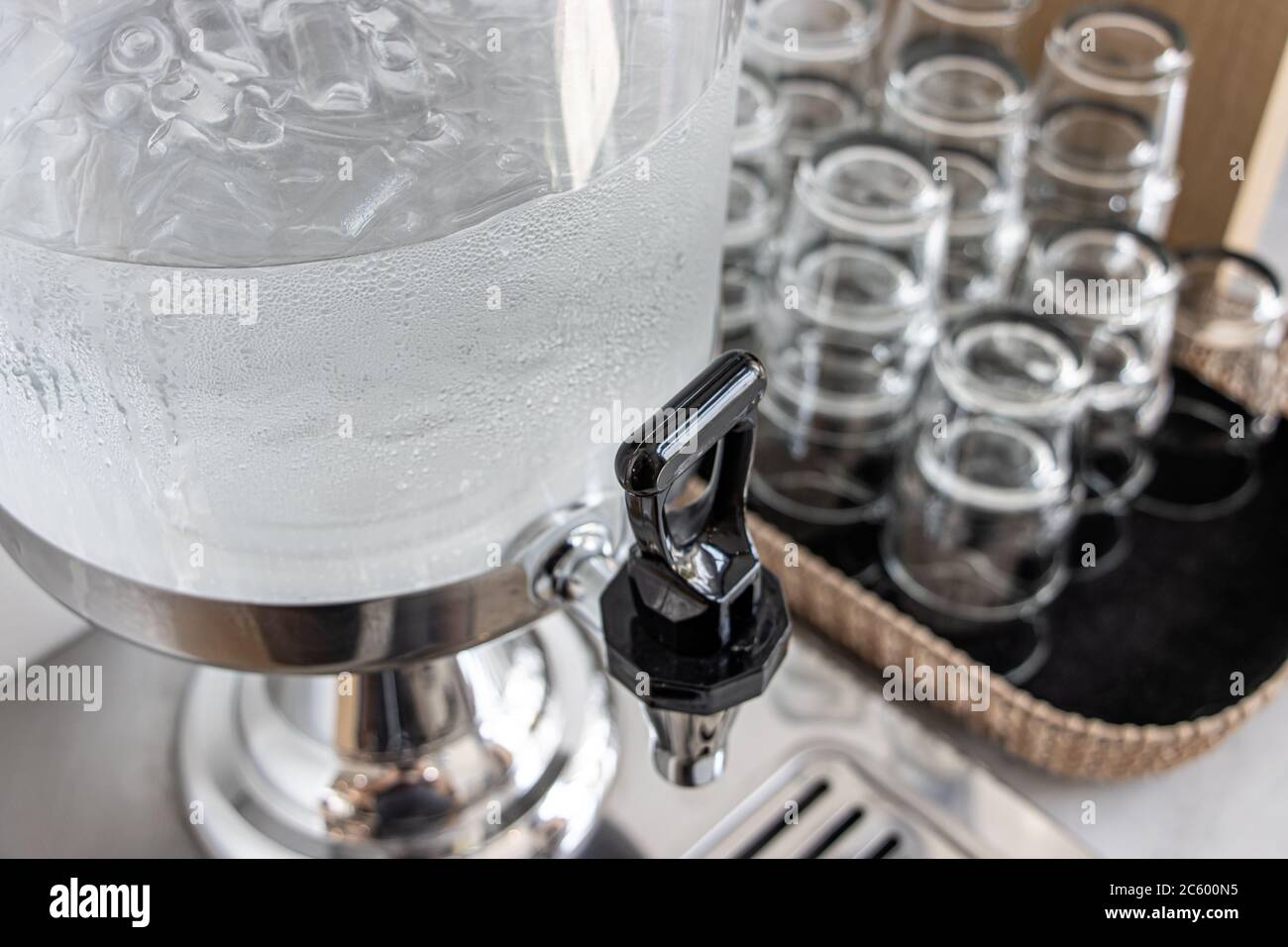 Pulire l'acqua potabile con ghiaccio in un dispenser self-service con vetro sul tavolo. Rubinetto da contenitore di vetro per acqua fredda al buffet self service Foto Stock