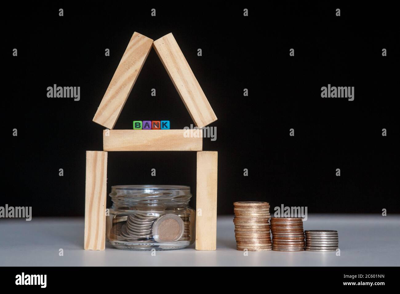 Banca di vetro con molte monete del mondo, parola o etichetta della casa su vaso di denaro e blocchi geometrici della casa di legno sopra la tabella Foto Stock
