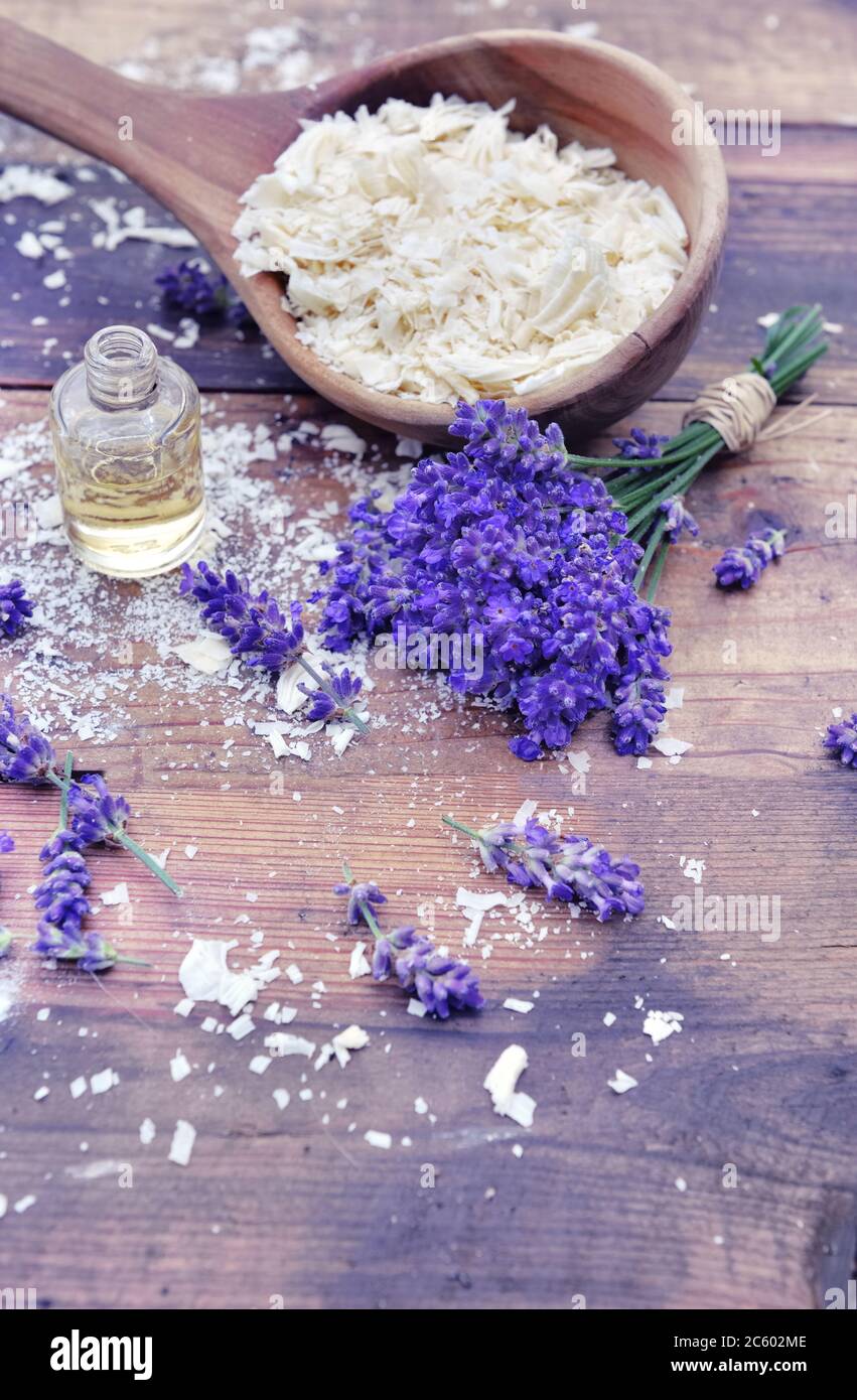 cucchiaio pieno di fiocchi di sapone con olio essenziale e mazzetto di fiori di lavanda su sfondo di legno Foto Stock