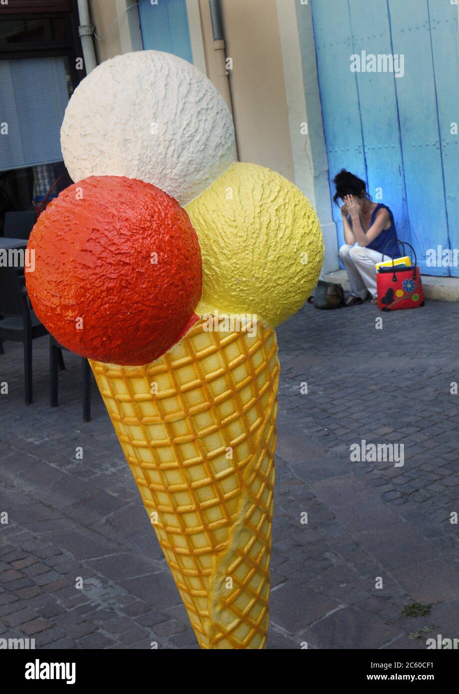 Una donna parla sul suo telefono dietro una grande pubblicità gelato coni scultura. Foto Stock