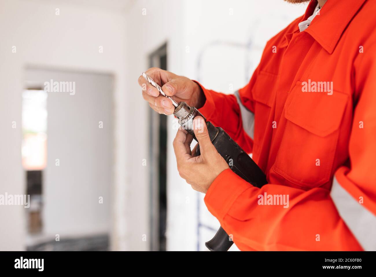 Primo piano costruttore in abiti da lavoro arancioni che tengono la macchina perforatrice dentro Foto Stock