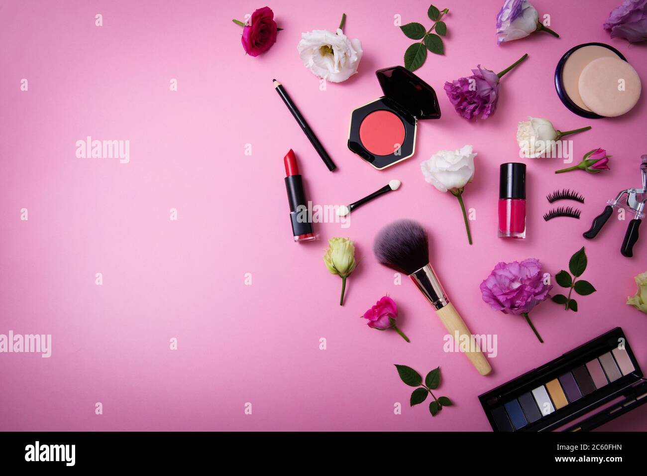 cosmetici per il trucco e attrezzature con fiori su sfondo rosa con spazio per la copia. vista dall'alto Foto Stock