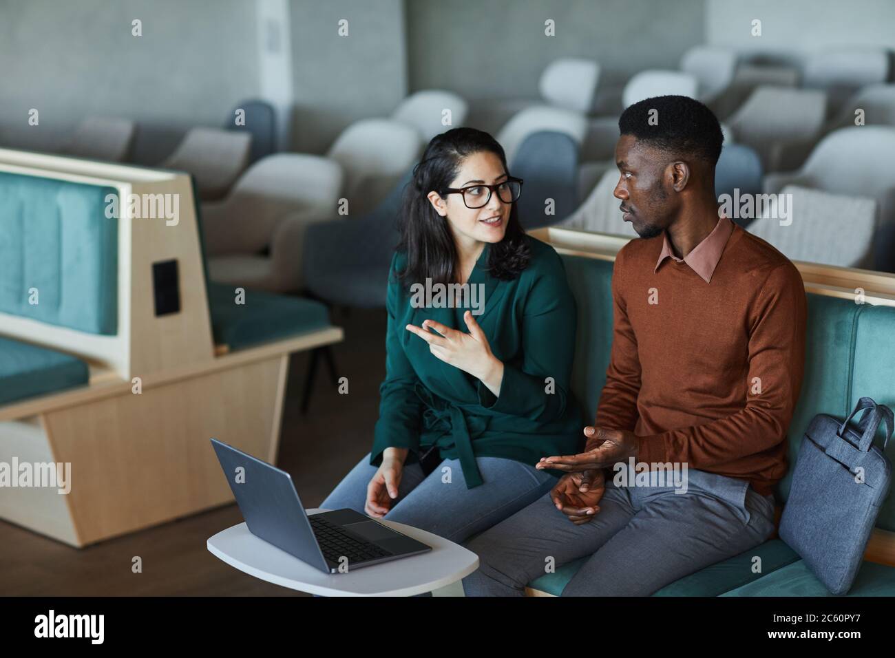 Ritratto di giovane donna contemporanea che indossa occhiali che parlano con l'uomo afroamericano e gesturing attivamente mentre discute progetto in auditori vuoto Foto Stock