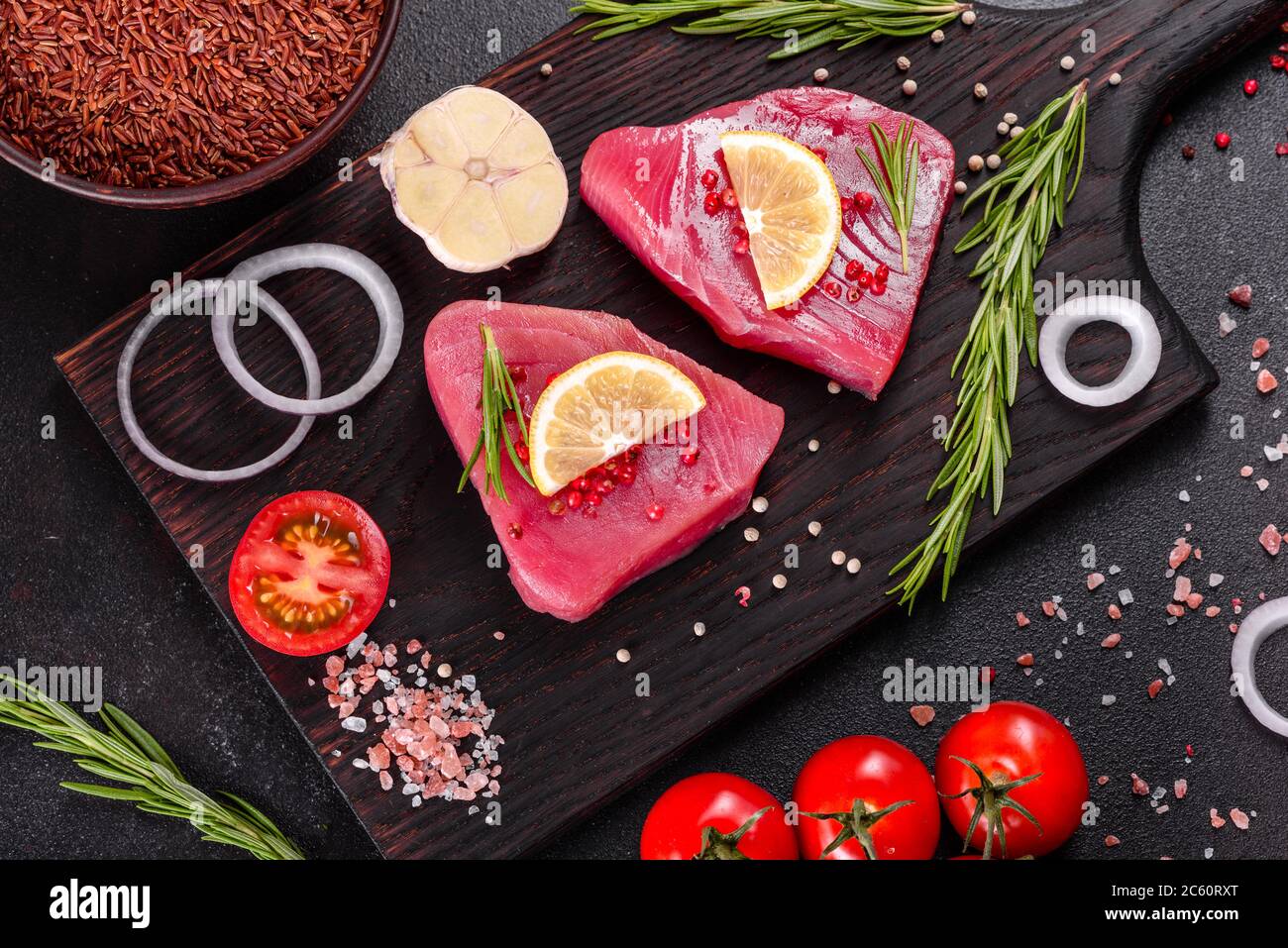 Bistecche di filetto di tonno fresco con spezie ed erbe su fondo nero. Preparare il tonno per la cottura Foto Stock