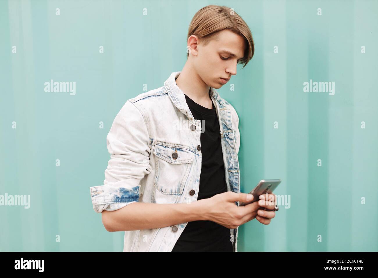 Ritratto di giovane uomo pensieroso in piedi e utilizzando il suo cellulare su sfondo blu Foto Stock