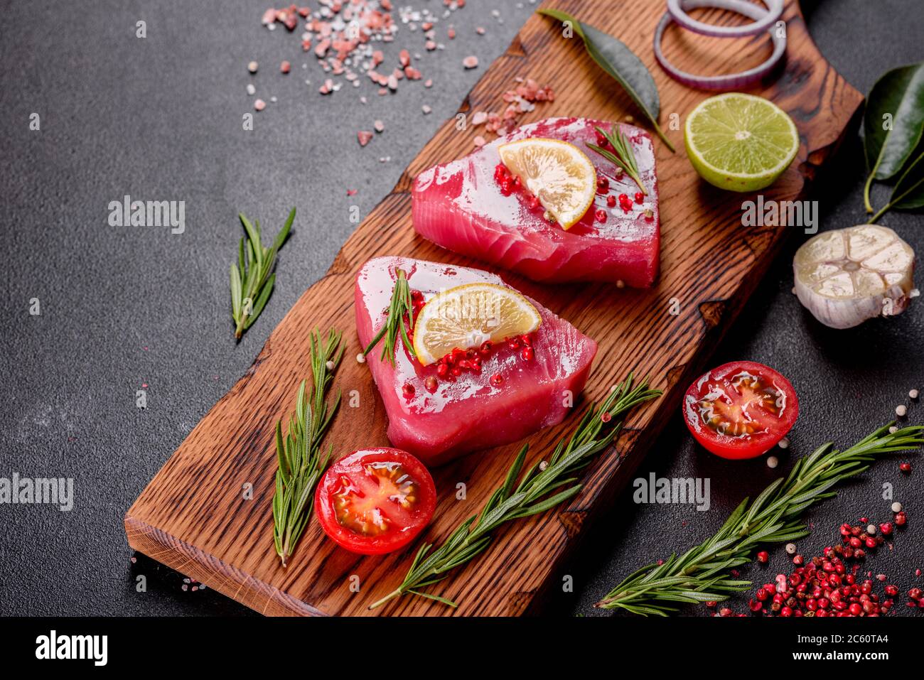 Bistecche di filetto di tonno fresco con spezie ed erbe su fondo nero. Preparare il tonno per la cottura Foto Stock