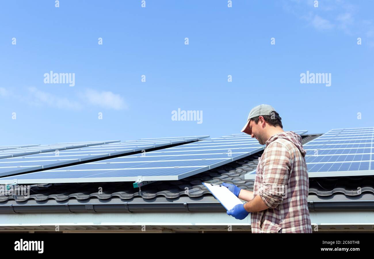 Energia solare pannello. Ingegnere elettrico uomo sta lavorando per controllare i documenti in stazione solare contro il tetto della casa e cielo blu. Sviluppo sole Foto Stock