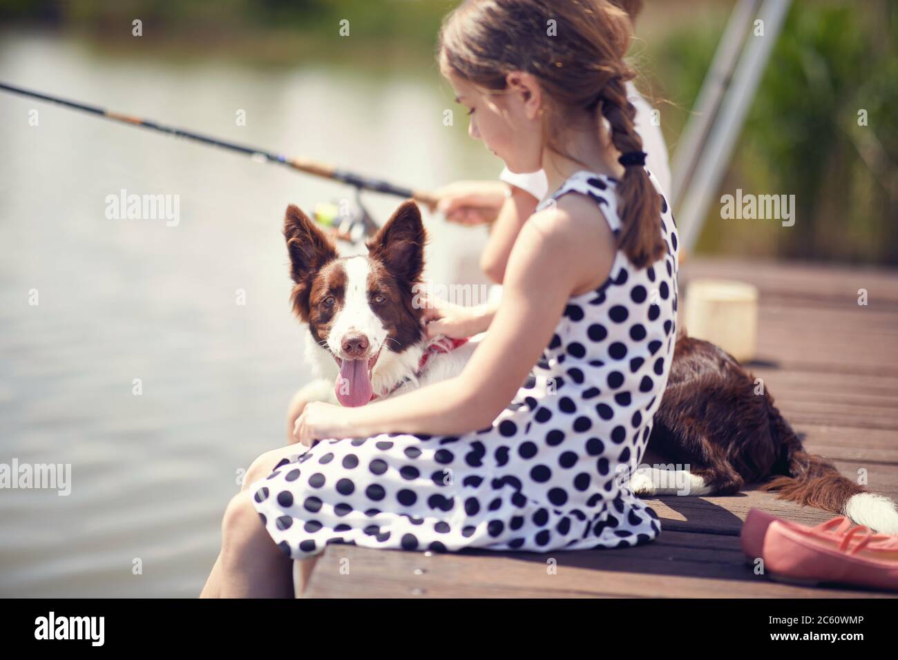 Bambina seduta su un molo di legno e godendosi con il suo cane. Foto Stock