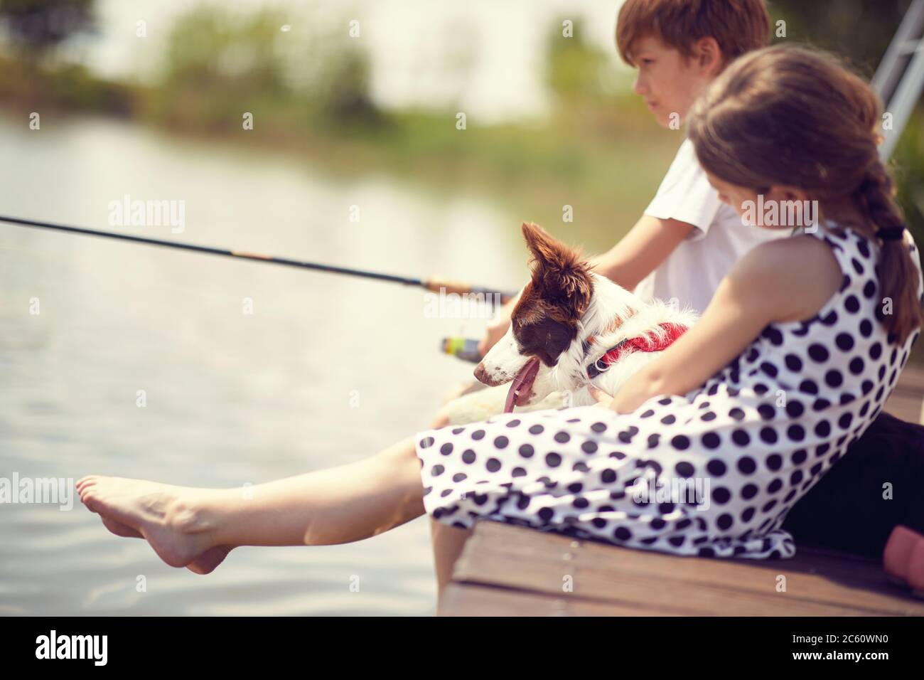Bambini piccoli con il cane seduto su un molo di legno e la pesca in un laghetto. Foto Stock