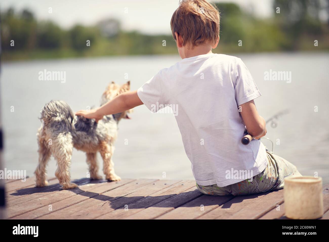Ragazzo seduto su un molo di legno e godendosi con il suo cane e la pesca. Foto Stock