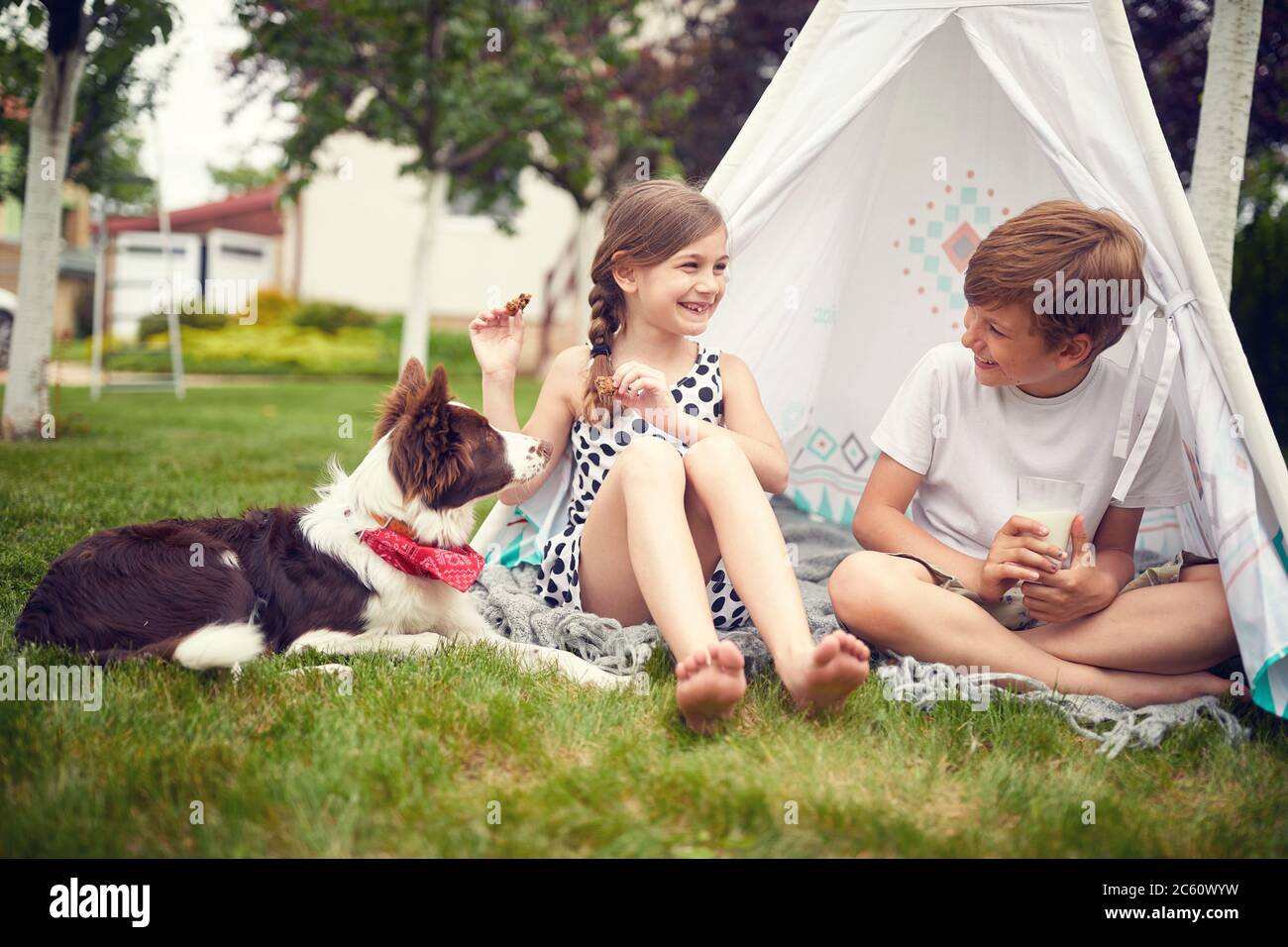 Sorridente bambini che giocano in cortile con il cane in teepee e mangia biscotti. Foto Stock
