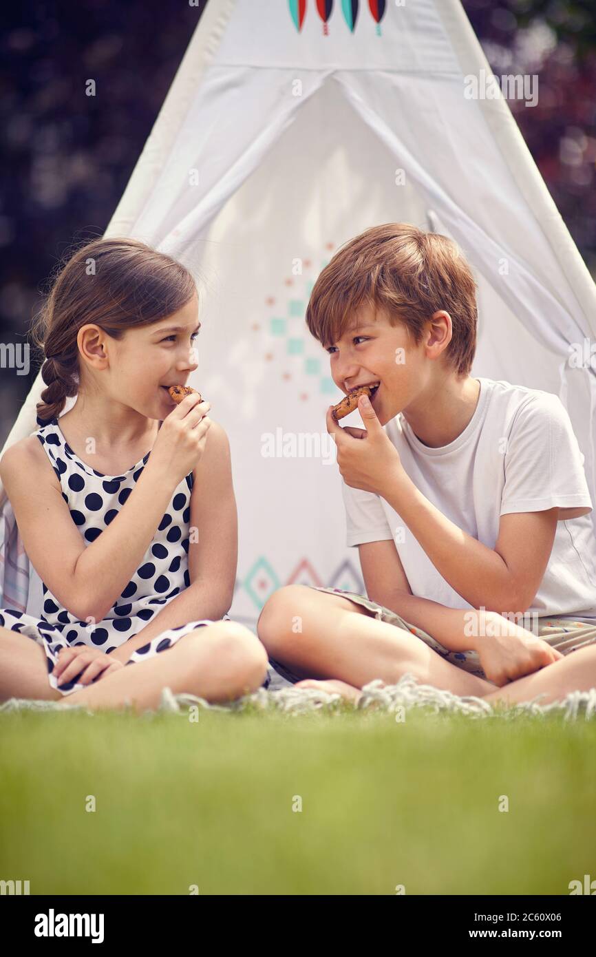Carino felici bambini seduti in teepee in cortile e mangia biscotti. Foto Stock